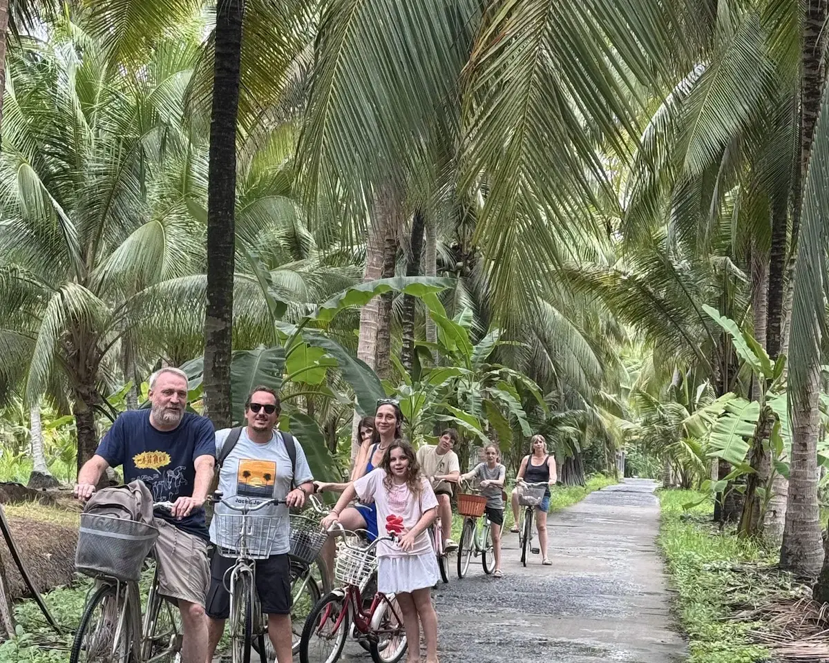 Guests cycling along a narrow coconut village lane near Coco Happy Farm