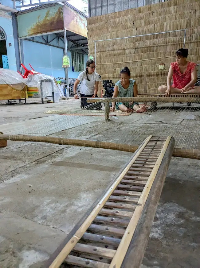 A visitor with local mat weavers at a traditional loom